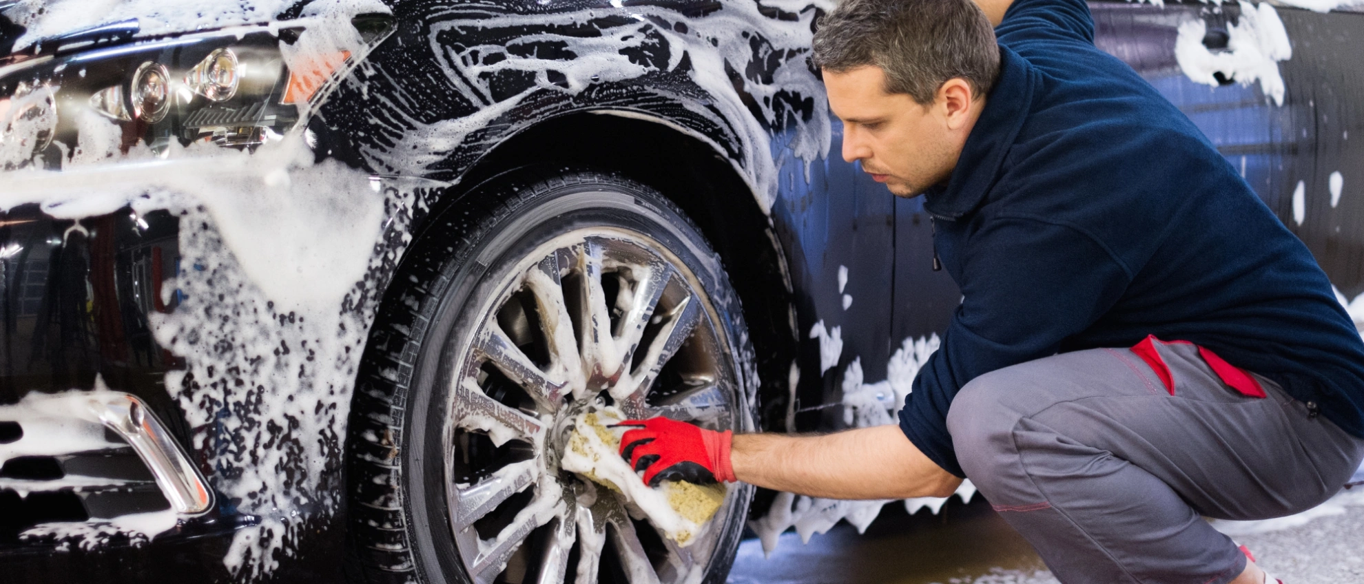 Mann reinigt die Felge eines schwarzen Autos mit Schwamm und Schaum